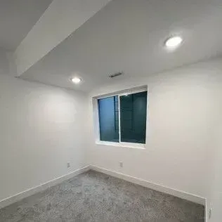 Empty, white-walled room with a window, recessed lighting, and gray carpet.