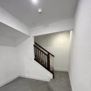 White-walled room with stairs and dark wood banister. Gray carpet and bright ceiling.