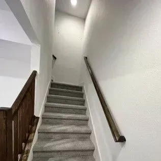 Staircase with gray carpeted steps, white walls, and wooden handrails.
