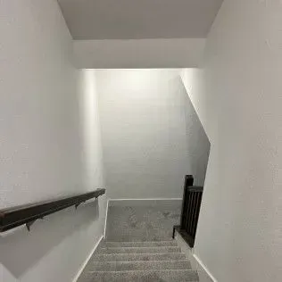 Stairwell with gray carpeted stairs, white walls, and a dark wooden handrail and banister.