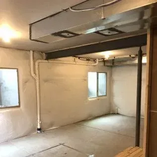 Empty basement with two windows, concrete floor, and exposed pipes.