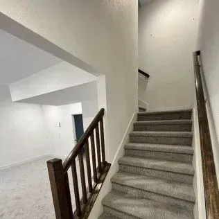 Staircase with carpeted steps and wooden railing leads to an upper level, with an open doorway to a room below.