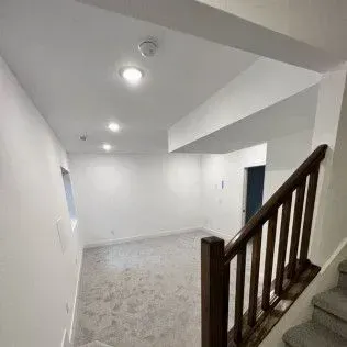 Staircase leading to a finished basement with white walls, recessed lighting, and carpet flooring.