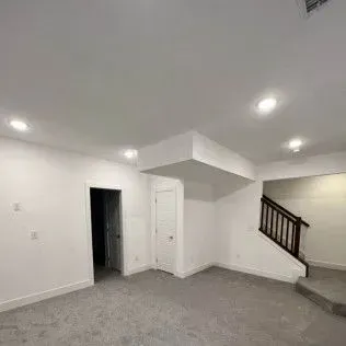 Empty interior room with recessed lighting, door, and staircase. White walls, grey carpet.