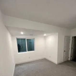Empty room with white walls, carpeted floor, window, and doorway.