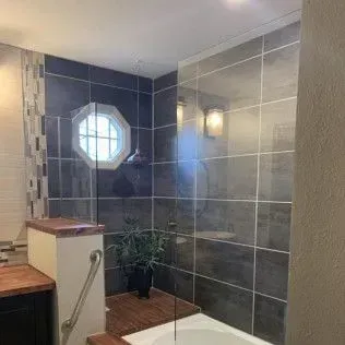 Bathroom with dark gray tiled walls, octagonal window, shower, and a small plant.