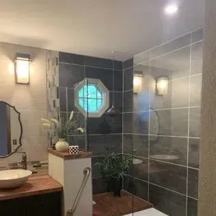 Bathroom with dark gray tile walls, octagon window, vanity, and shower.