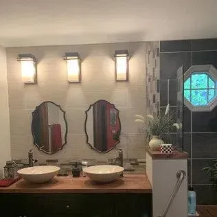 Bathroom with two sinks, mirrors, and sconces. Features a wood countertop and octagonal window.