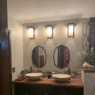 Bathroom with two sinks, oval mirrors, and sconce lighting above.