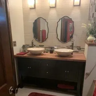 Bathroom with a black double vanity, two vessel sinks, ornate mirrors, and warm lighting.