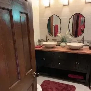 Bathroom with double sink vanity, oval mirrors, and burgundy accents.
