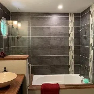 Bathroom with gray tile, tub, and wooden vanity.
