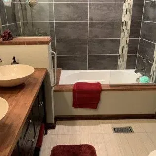 Bathroom with wood vanity and tub surround, featuring dark gray tile and red accents.