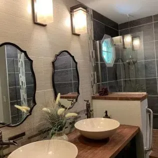 Bathroom with two sinks, mirrors, and shower behind a glass door. Neutral colors, modern style.