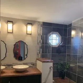 Bathroom with mirrors, dark tile, vessel sink, sconces, and a window.