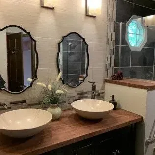 Bathroom with two bowl sinks, oval mirrors, and wood countertop.