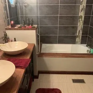 Bathroom with white sinks, tub, dark tile wall, and wooden accents.