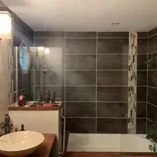 Bathroom with dark gray tiled walls, white sink, and shower/tub area.