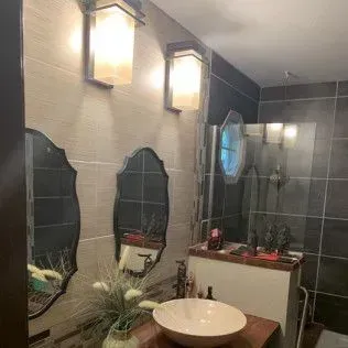 Bathroom with two sconces, mirrors, and a vessel sink. Tile walls and a shower are visible.