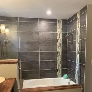 Bathroom with dark gray tile, white bathtub, and decorative vertical tile strip.