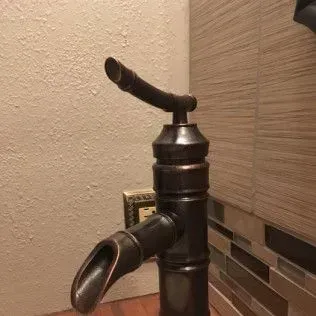 Bronze bathroom faucet with a curved spout and handle. Beige and tile wall background.