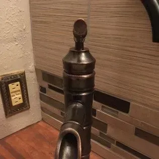 Close-up of a bronze faucet against a tile backsplash and a wooden surface.
