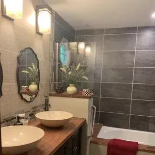 Bathroom with dark gray tile walls, two vessel sinks, a bathtub, and floral arrangements.