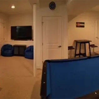 Basement rec room: Pool table, TV, bean bag chairs, door, small table with stools, tan carpet.