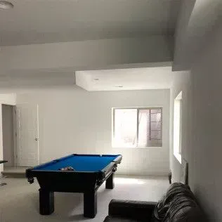 Pool table in a white-walled room with a window, a door, and a black leather sofa.
