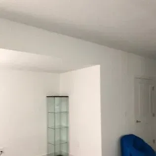 White room with a glass display case, a blue chair, and a white door.