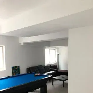 Pool table and a couch in a room with a low ceiling and two windows.