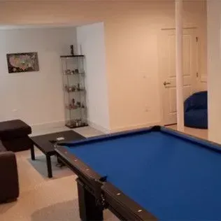A basement with a pool table, seating area, glass display case, and open doorway.