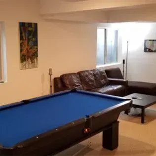 A pool table with a blue felt top, a leather sofa, and a painting in a brightly lit room.