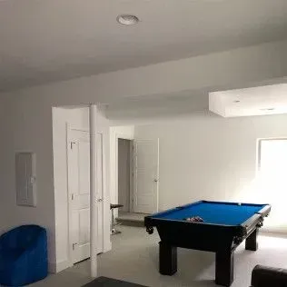 A finished basement with a blue pool table, white walls, and a beanbag chair.