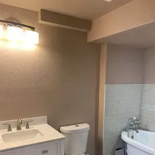 Bathroom with a white vanity, toilet, and bathtub. The walls are painted in shades of tan and pink.