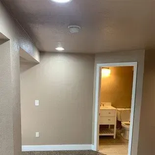 Interior hallway with doorway to bathroom; tan walls, recessed lighting, and a partially visible bathroom.