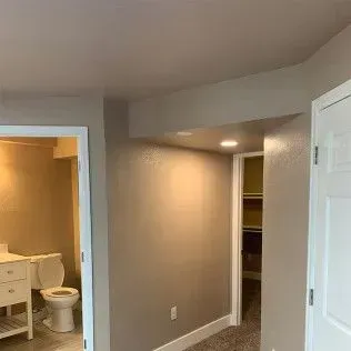 Interior view of a room with doorways to a bathroom and closet, neutral walls, and white doors.