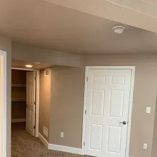 Interior view of a room with a white door, closet, and carpeted floor. Beige walls and a white ceiling.
