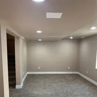 Empty beige-painted room with carpet, recessed lighting, and an open doorway to a staircase.