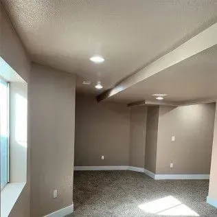 Basement interior with tan walls, carpet, and recessed lighting. A window is on the left.