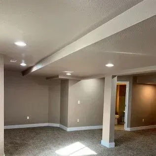 Finished basement with carpet, neutral-colored walls, and recessed lighting. A support beam divides the space.