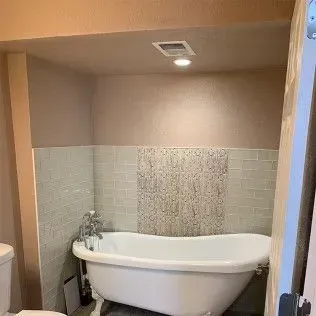 Clawfoot bathtub in a tiled alcove, with light-colored walls and a recessed light.