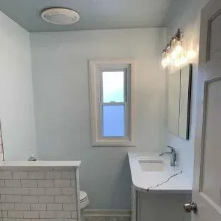 Bathroom with white vanity, window, mirror, and white subway tile wall. Light blue walls.