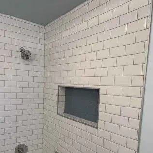 White tiled shower with a built-in shelf and silver shower fixtures.