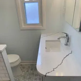 Bathroom with white countertop, sink, and chrome faucet. Includes a toilet, window, and light blue walls.