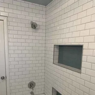 White tiled shower with a niche and showerhead.