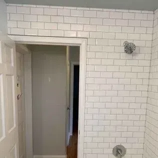 White tiled shower surround with door to adjacent room.