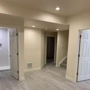 Interior of a newly renovated room with beige walls, gray floor, white doors, and recessed lighting.