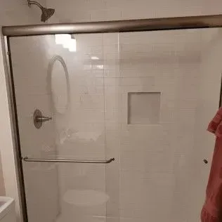 White-tiled shower with a sliding glass door and a showerhead. A towel hangs on the right.