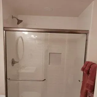 Shower with a glass door, white tiled walls, and bronze fixtures. A pink towel hangs to the right.
